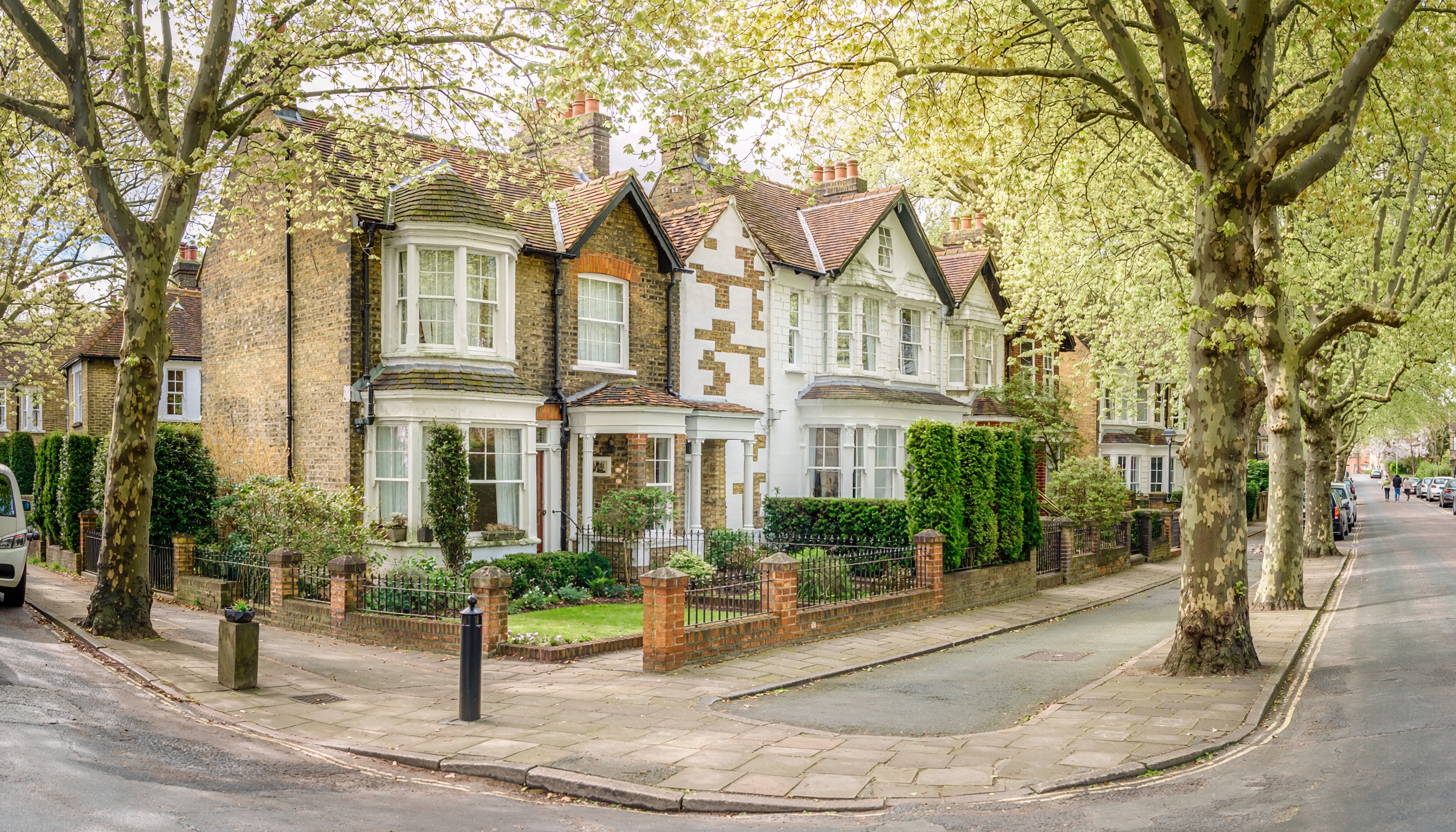 Quiet residential street with semi-detached brick houses, bay windows, and fresh green trees lining the sidewalk.”