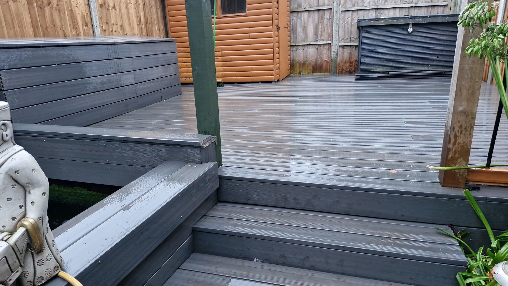 Modern grey composite decking with clean lines and a low-maintenance finish. The raised deck features wide steps, built-in seating, and a neat garden shed backdrop, showcasing how composite decking enhances outdoor living spaces with durability and style.