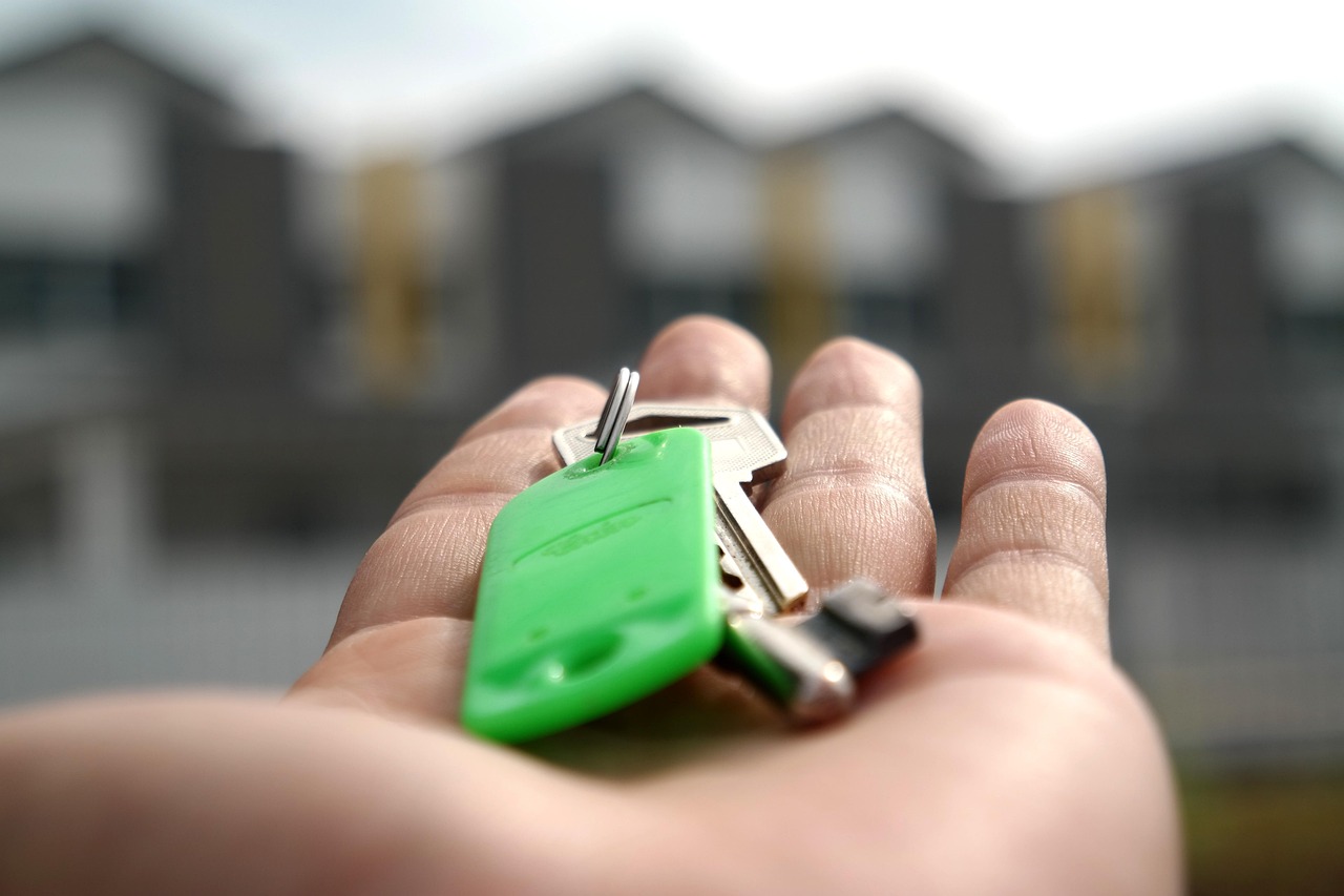 Close-up of a hand holding house keys with a green key fob in front of modern homes, symbolising successful property sales and the confidence vendors gain when working with a trusted and honest estate agent in Orpington.