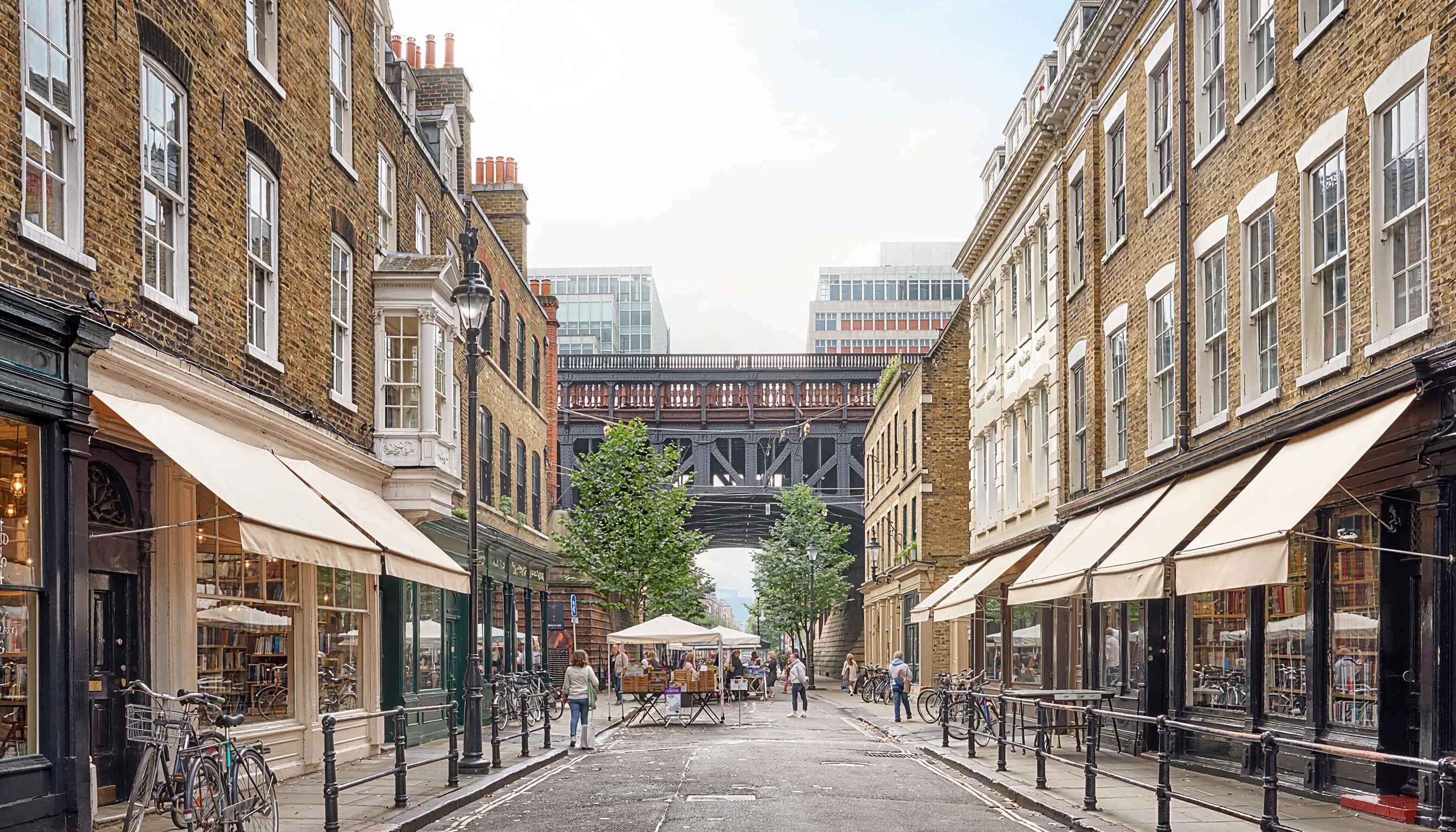 Charming urban street with historic brick buildings and beige awnings, bicycles parked along sidewalks, people walking and browsing outdoor market stalls under white canopies, with an iron bridge overhead and modern glass buildings beyond.