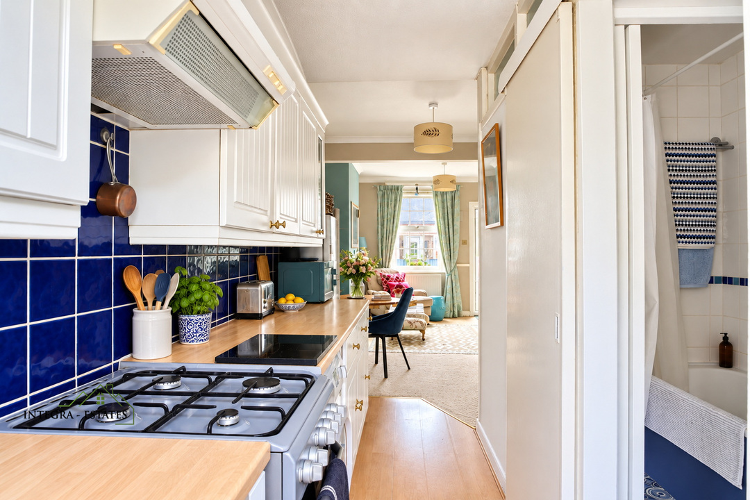 Galley-style kitchen with white cabinetry, blue tiled splashback, gas cooker, and wooden worktops, leading through to a bright open-plan living and dining area.