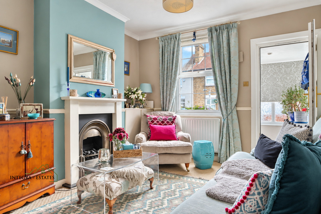 Cozy living room with a feature fireplace, armchair, sofa, patterned rug, and large window with curtains, decorated in soft neutral tones with blue accents.