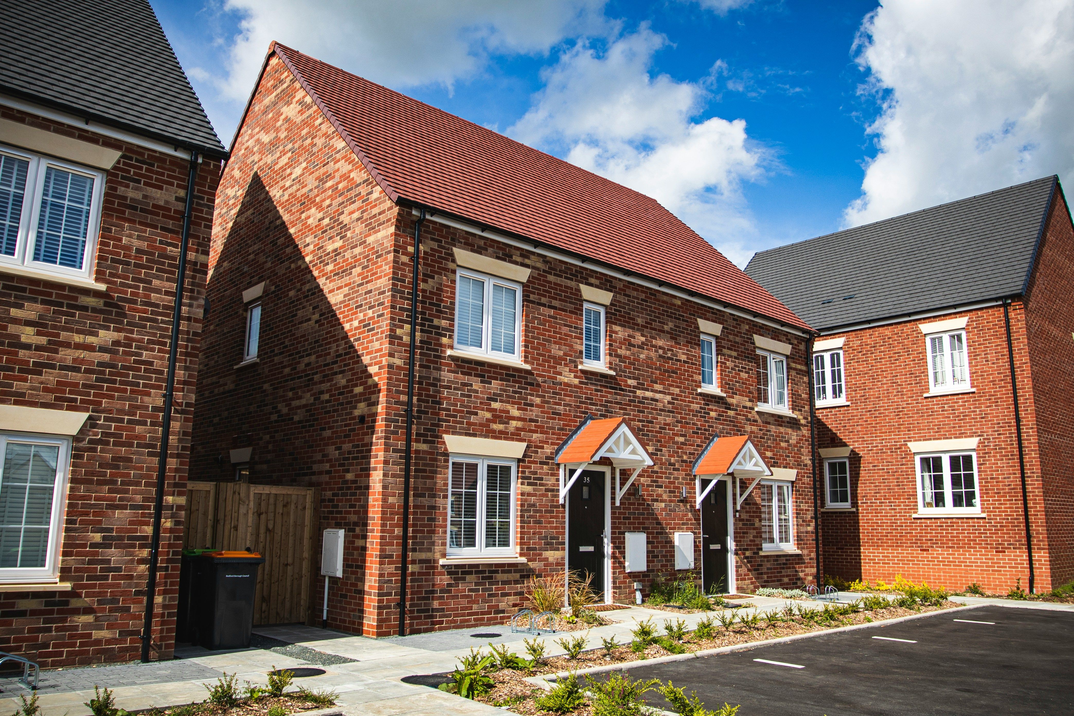 Row of modern brick townhouses with white-framed windows, pitched roofs in red and dark gray tiles, and small gabled porches above each front door.