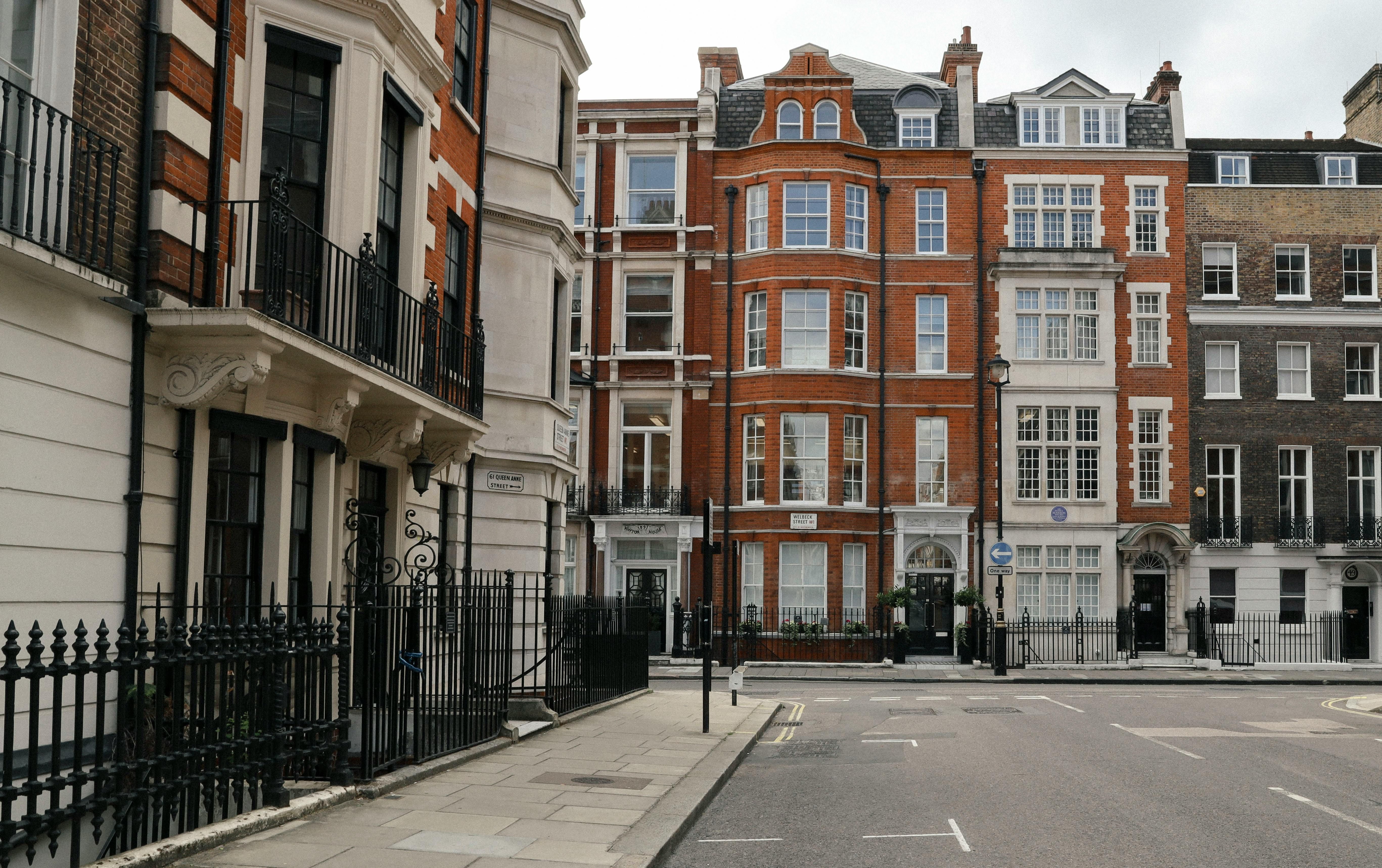 A quiet London street lined with historic red brick and white stone buildings, featuring wrought iron balconies, large sash windows, and classic street lamps.